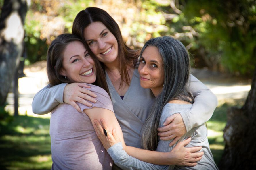 Three women hugging and smiling outdoors